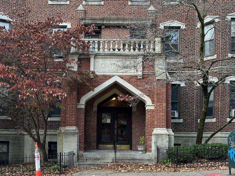A brick Allston building with a stone base and a balcony over the entrance